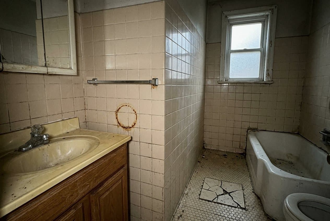 Outdated grimy bathroom with cracked floor tile and rust stains
