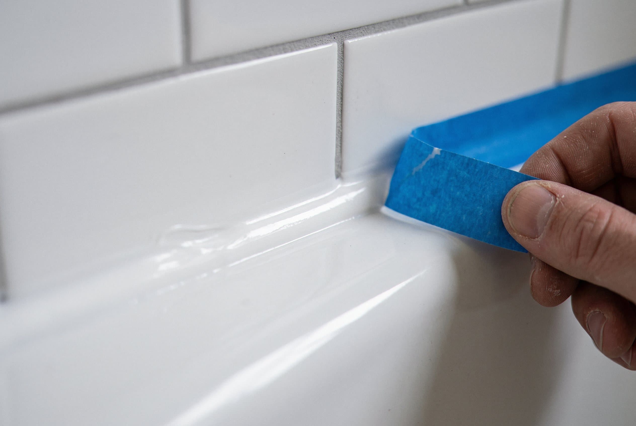 Applying fresh white caulk along a tub tile joint